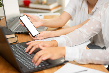 Mujer de negocios sostiene celular con sus manos mientras trabaja con su compañera en su oficina.