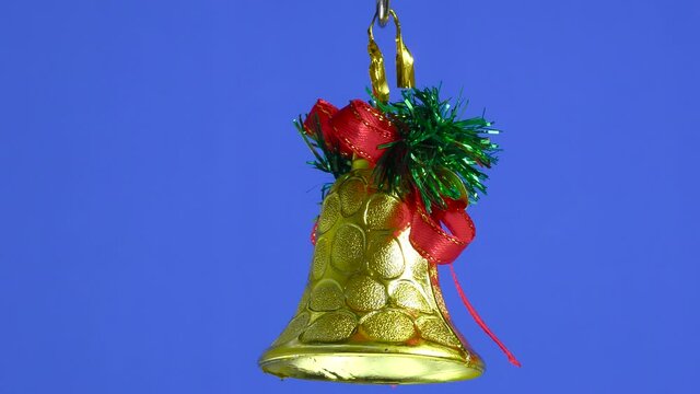 A golden Christmas bell is spinning on a blue plain background