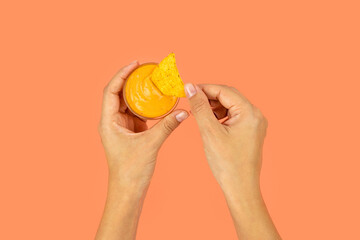 Woman's hands are holding cheese sauce with crispy nachos in a color photo.