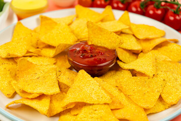 Mouth-watering nachos chips on a white plate and a spicy sauce for a delicious vegetable meal.