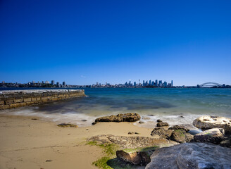Fototapeta na wymiar Sunny Spring day on Sydney Harbour with nice rocks in the foreground the soft waves crashing on the shore and the beautiful harbour foreshore as a backdrop NSW Australia