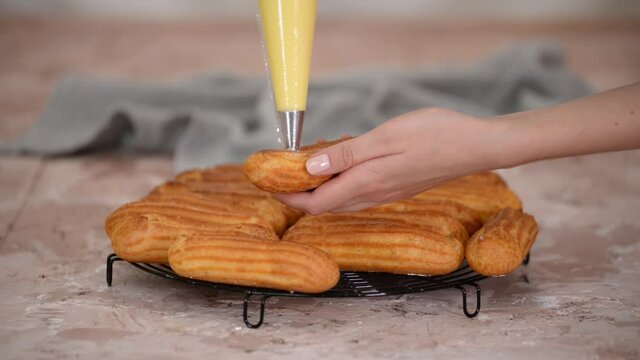 The pastry chef fills the eclairs with creams from a pastry bag.