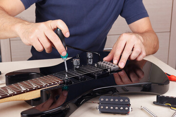 Fototapeta na wymiar Guitar master adjusts height pickups on modern electric guitar.