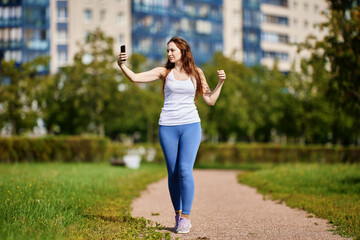 Young white woman takes pictures of herself jogging using smartphone.