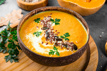 A bowl of homemade pumpkin soup with seeds, sesame seeds and flax seeds close-up, warm autumn food