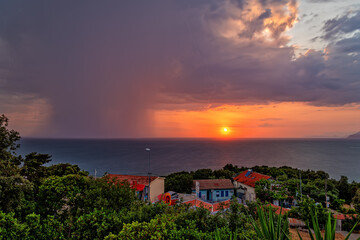 Sunset and rain at sea in the same photo. Sunlight and rainy clouds in the horizon at sea.