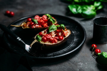 Eggplants with tomatoes, basil and cheese on a black plate