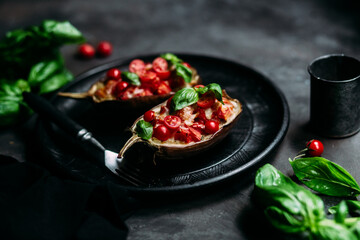 Eggplants with tomatoes, basil and cheese on a black plate