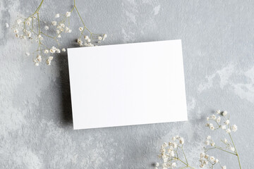 Invitation or greeting card mockup with white gypsophila twigs. Blank card mockup on grey...