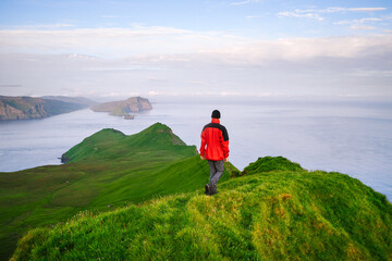 Fototapeta premium A tourist walks through the green hills on Mykines island, Faroe Islands