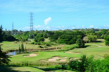 View of Golf Course with putting green, green grass, sand bunker, blue sky, and high voltage electric transmission tower background. Using for Golf field banner with a copy for your text.