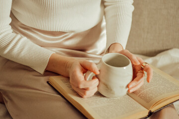 woman reading a book with cup of tea or coffee. a woman holds a book on her lap