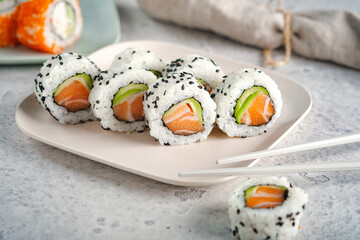 A set of fresh sushi rolls with salmon, avocado and black sesame seeds served on a plate with chopsticks.  California roll
