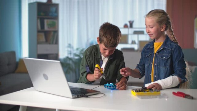 smart kids play with screwdrivers, boy and girl with tools repair mini quadcopter next to laptop at table