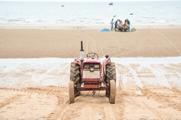 Tractors waiting to haul a local fishing boat out of the sea at low tide at Jomtien Beach, Pattaya, Thailand