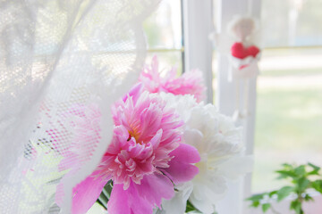 Peonies stand by the window white tulle curtains.