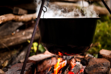 Close-up of a black pot of hot, steaming soup outdoors. Hiking and campfire cooking with bright orange sparkles, selective focus.