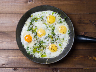 Fried eggs in a frying pan on a plank background. Delicious breakfast. View from above