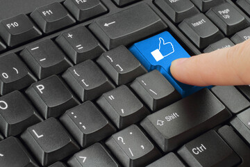 Finger pushing blue social media button on black keyboard