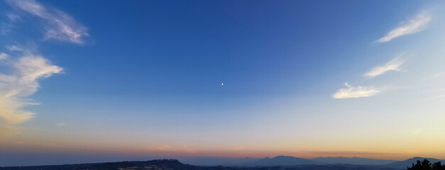 Tramonto estivo sui monti Appennini con la Luna nel cielo azzurro limpido