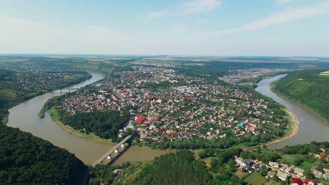 Panorama of city Zalishchyky. Nature and city landscape. Winding horseshoe-shaped river across which bridge is built. Hill with forest and vegetation and valley with buildings. Skyline with blue sky