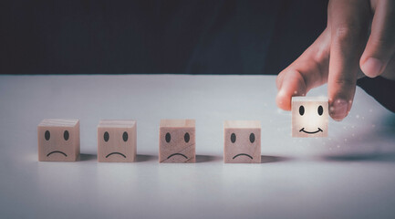 Customer service evaluation and satisfaction survey concepts. Customer hand hold the happy face smile face icon  on wooden cube on wooden cube on table.