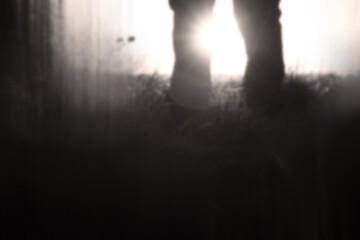A close up of a mans legs silhouetted by the sun. With a blurred, out of focus, sepia edit.