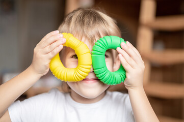 anti stress sensory pop tube plastic toy in kid's hands. a little happy child boy plays with a poptube fidget toy at home. children holding and playing pop tube yellow and green color, trend 2021 year - obrazy, fototapety, plakaty