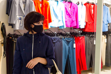A woman in a black protective mask goes shopping, looking at things, shopping.