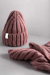 Small red knitted hat with on a white scarf jn grey background. woolly hat Closeup.