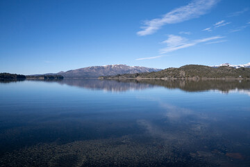 Obraz premium The lake in a sunny morning. Panorama view of the forest, lake and the perfect reflection of the sky in the blue water. The Andes mountain range in the background.