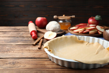 Raw dough and ingredients on wooden table, space for text. Baking apple pie