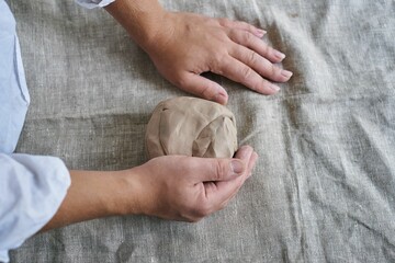 closeup female hands kneading a piece of clay on the table
