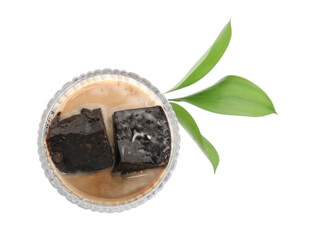 Glass of milk with grass jelly and green leaves on white background, top view