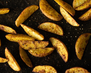 Many cooked and crispy potato wedges seasoned with salt and pepper resting on a metal oven tray