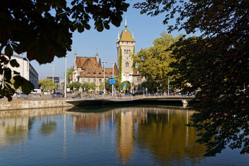 Fototapeta na wymiar National Landes Museum Zurich, view limmatquai to Walche Bridge on an autumn morning, building and spire between trees against blue sky, wide angle shot