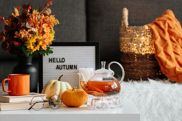 Still-life. A blanket, pumpkins, a teapot and a cup of tea on the coffee table in the home interior of the living room. A cozy autumn concept.