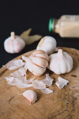 
Garlic bulb on a wooden board on a black background, with dried garlic. Condiments and spices in the kitchen. Selective focus.
