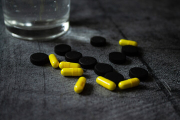 glass of water, yellow pills, black background