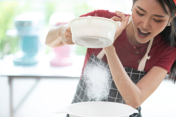 young woman housewife sifting flour from sieve in the kitchen