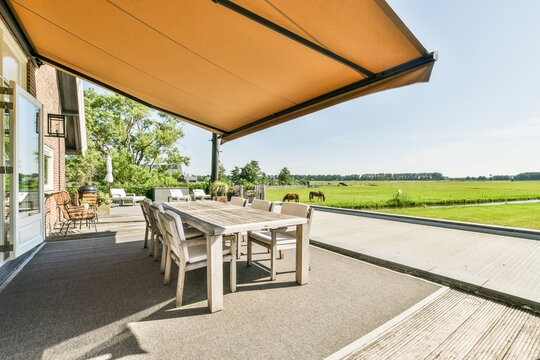 Terrace with furniture under canopy against horses grazing in pasture