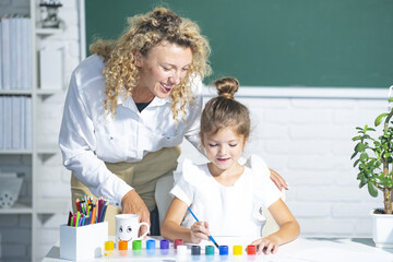 Teacher with young school kid in classroom. Mother and daughter learning.