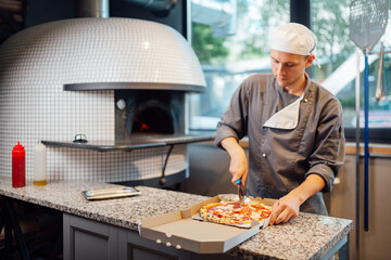 Cook slices pizza in a box. Catering kitchen work.