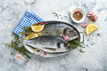 Raw dorado fresh fish or sea bream with ingredients for making lemon, thyme, garlic, cherry tomato and salt on light grey slate, stone or concrete background. Top view with copy space.