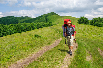 A male tourist with a large backpack climbs a mountain stone path high in the Carpathian 