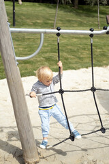 Little caucasian blond boy playing on kids playground in a sunny autumn day