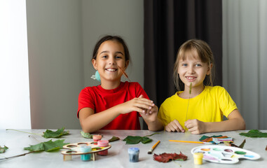 two girls paint autumn leaves at table.
