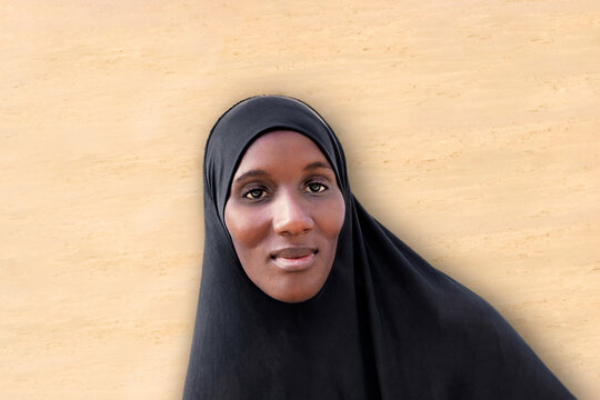 Beautiful African woman wearing a black veil in front of a  beige wall 