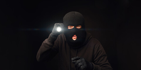 Masked burglar with flashlight on dark back - obrazy, fototapety, plakaty