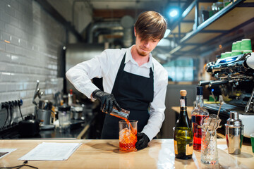 Barman pours drink ingredients into a mixing glass. Cocktail preparation process.